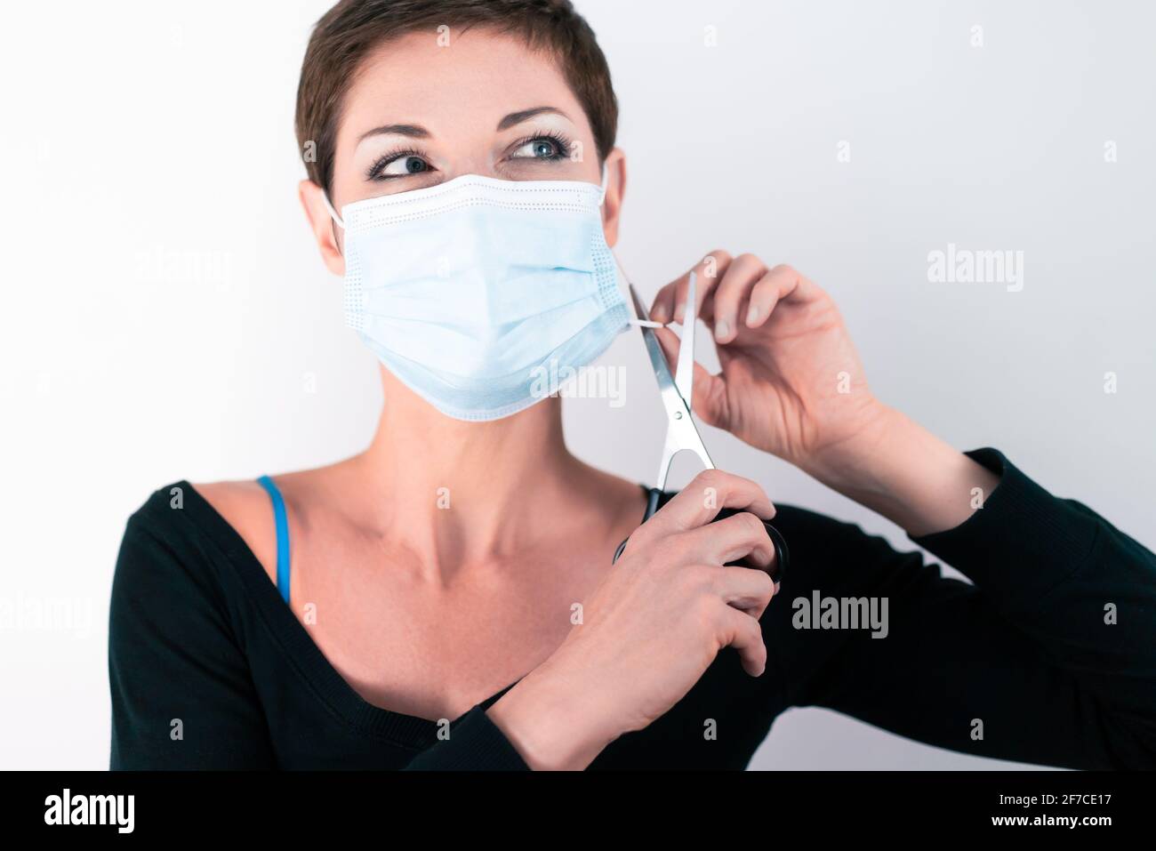 Schöne Frau mit kurzen Haaren, die ihre Gesichtsmaske mit einer Schere entfernt. Leben in Quarantäne. Umgang mit Einschränkungen des Coronavirus. Leben während einer Pandemie. Stockfoto