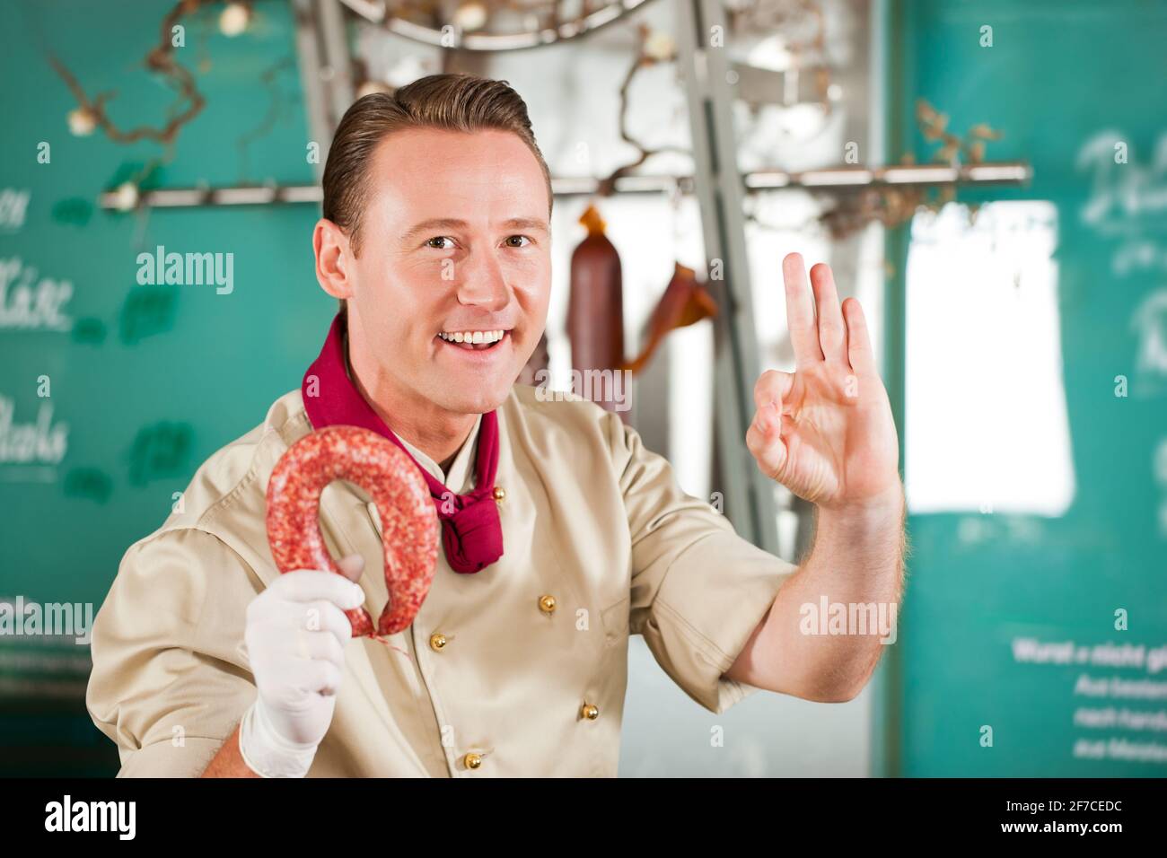 Portrait des Metzgers mit positivem Zeichen beim Halten der geräucherten Wurst Stockfoto