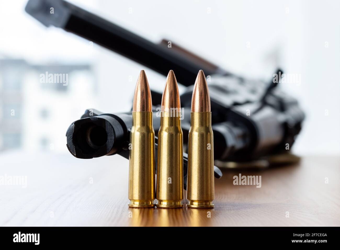 Drei Kugeln gegen verschwommene Kalaschnikow Sturmgewehr Hintergrund. Kartuschen im Kaliber 7.62 für ak 47 Nahaufnahme. Stockfoto