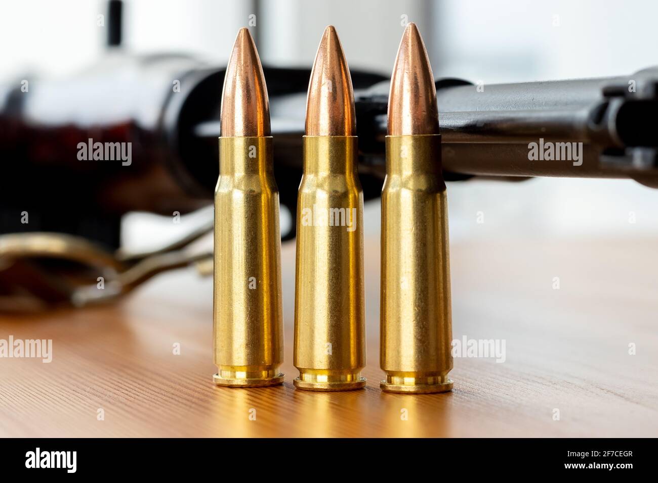 Drei Kugeln gegen verschwommene Kalaschnikow Sturmgewehr Hintergrund. Kartuschen im Kaliber 7.62 für ak 47 Nahaufnahme Stockfoto