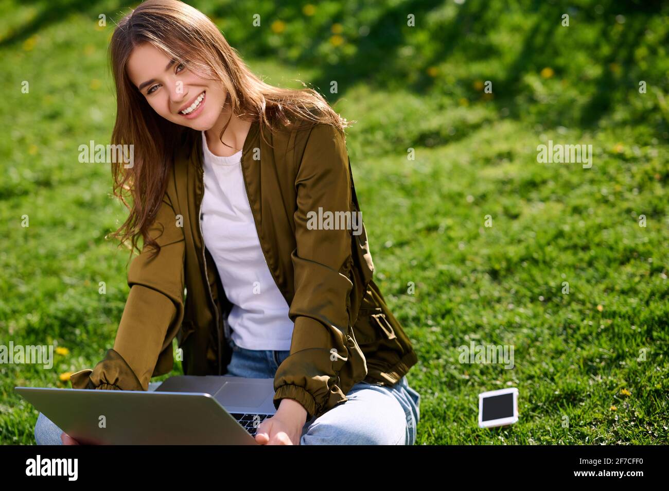 Lächelnde kaukasische Frau (Frau) arbeitet mit einem Laptop im Freien Sommerpark Stockfoto