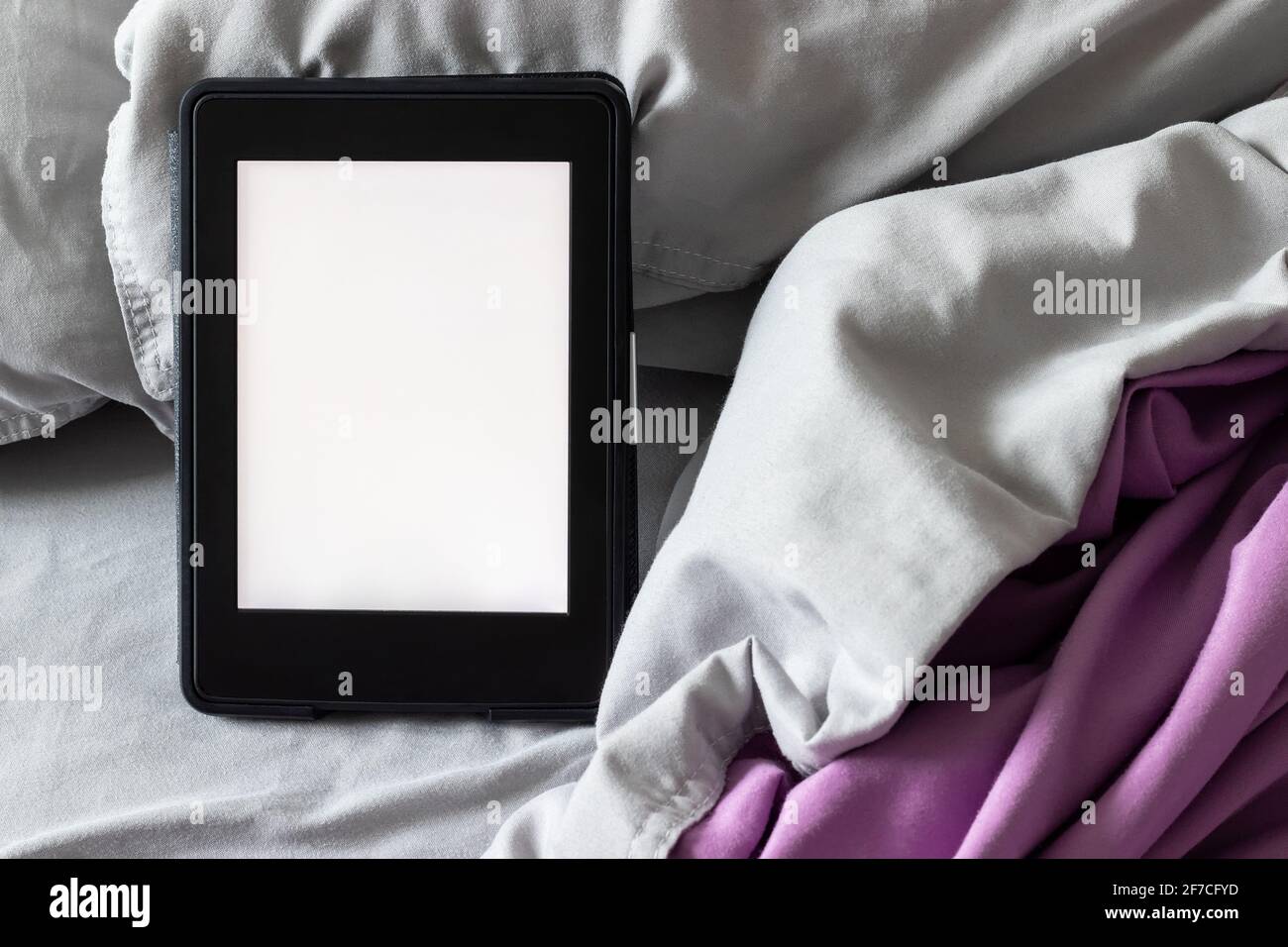 Ein modernes elektronisches E-Reader mit einem leeren Bildschirm auf einem grauen und violetten Bett. Mockup Tablet auf Microfaser-Bettwäsche Nahaufnahme Stockfoto