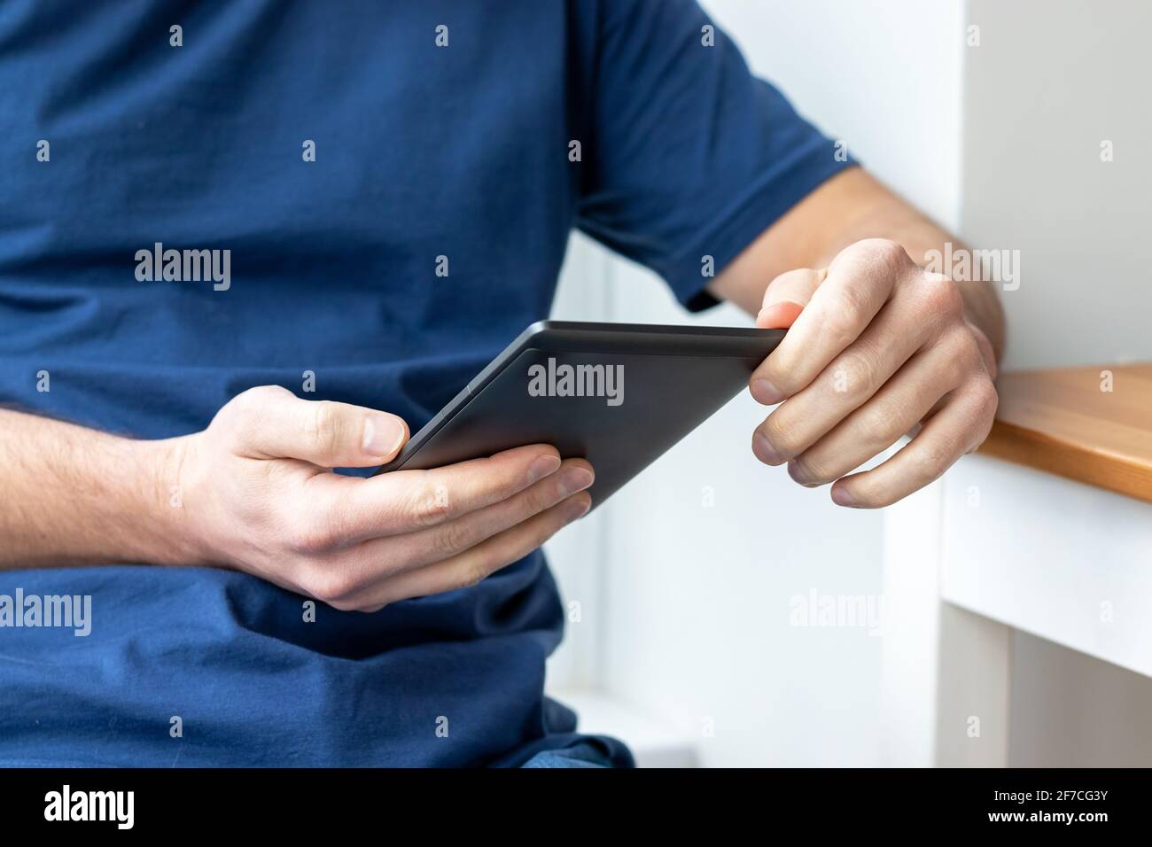 Graues elektronisches Buch mit E-Reader in männlichen Händen. Ein Mann in einem blauen T-Shirt mit einem Tablet. Selektiver Fokus Stockfoto