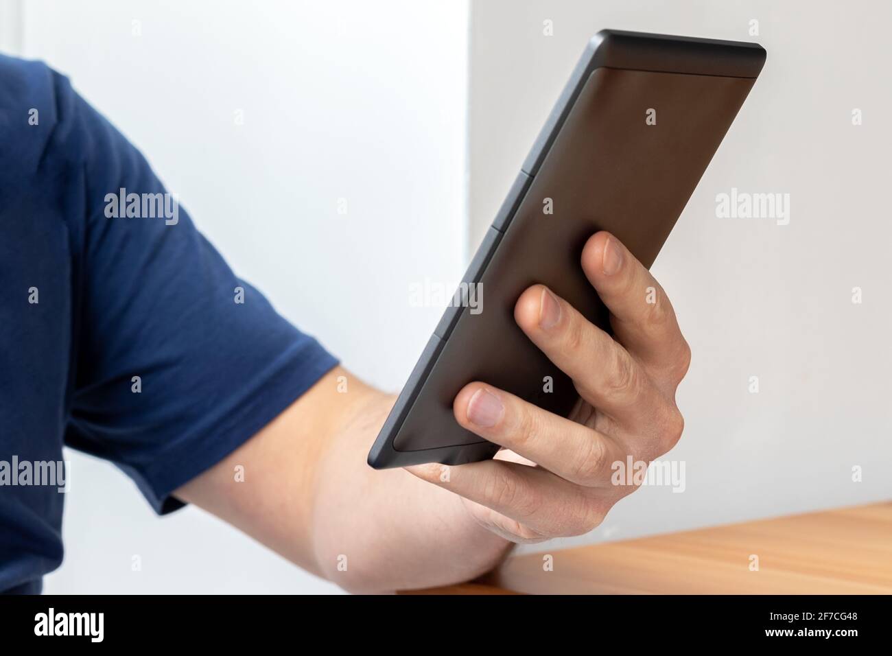 Graues elektronisches Buch mit E-Reader in männlicher Hand. Ein Mann in einem blauen T-Shirt mit einem Tablet. Selektiver Fokus Stockfoto