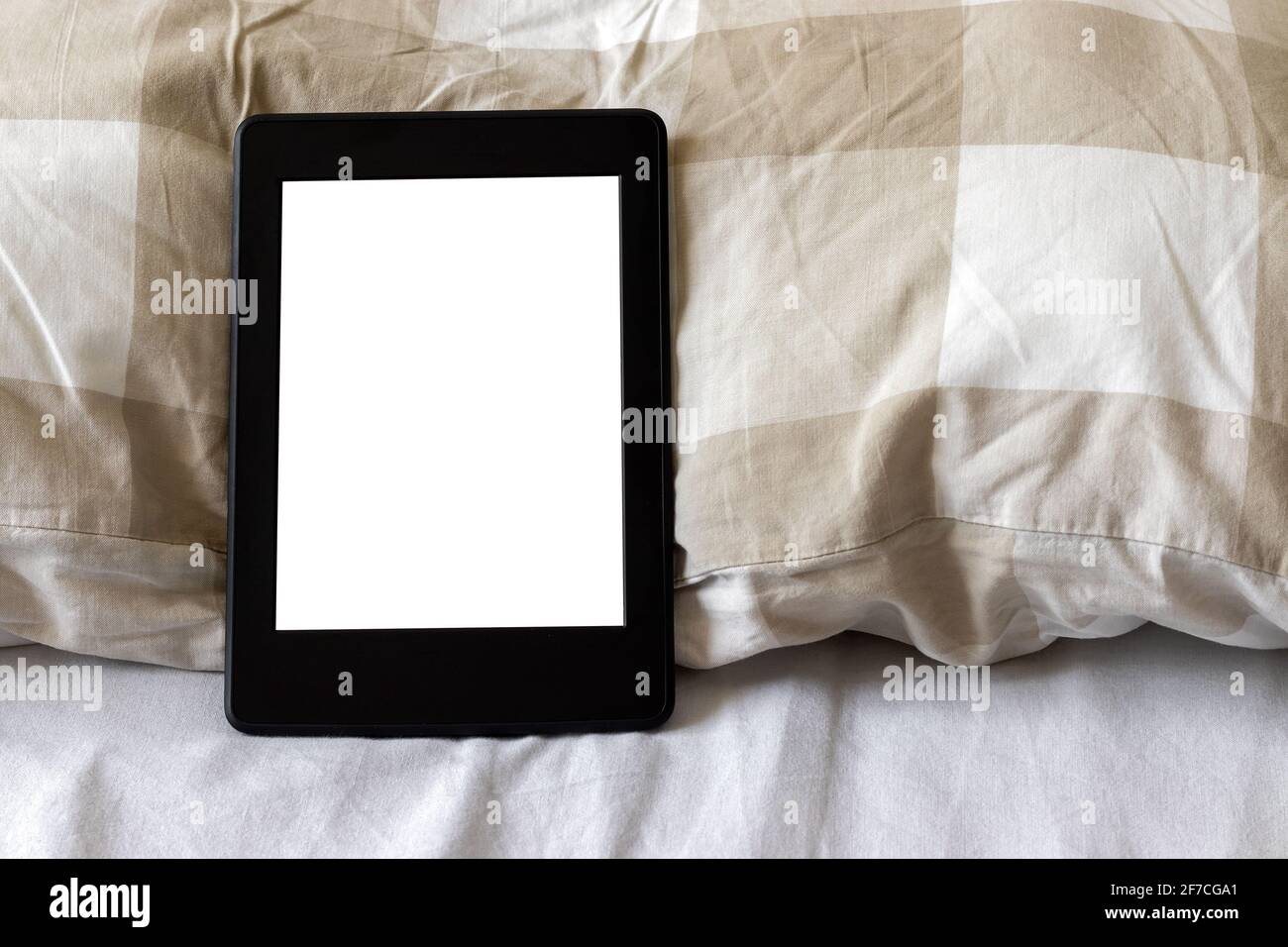Ein modernes schwarzes elektronisches Buch mit einem leeren Bildschirm auf einem weißen und beigen Bett. Mockup Tablet auf der Bettwäsche. Nahaufnahme Stockfoto