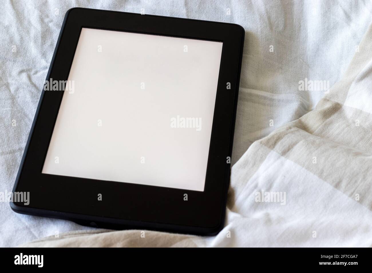 Ein modernes schwarzes elektronisches Buch mit einem leeren Bildschirm auf einem weißen und beigen Bett in Nahaufnahme. Mockup Tablet auf der Bettwäsche Stockfoto