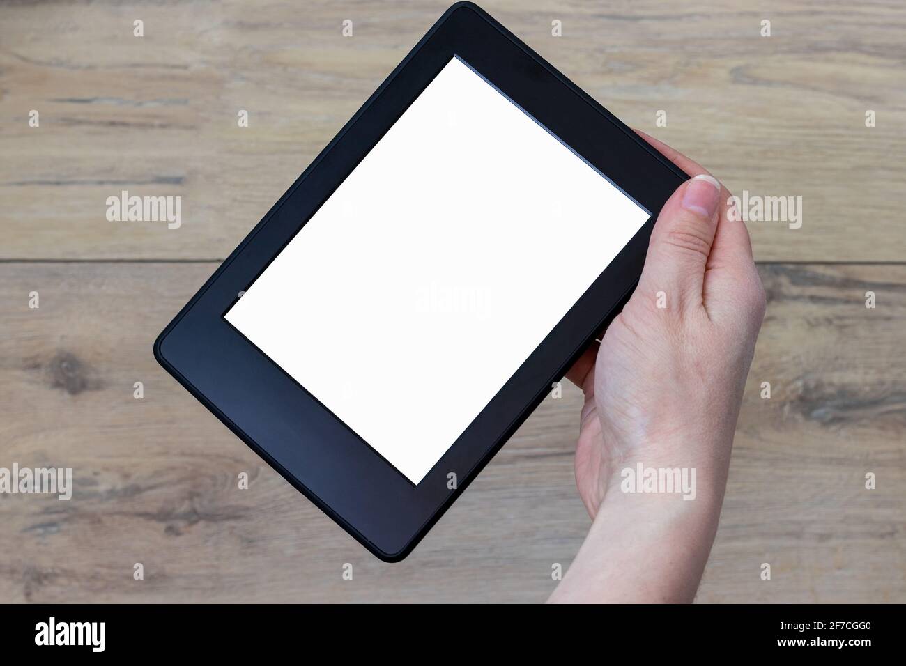 Ein modernes schwarzes elektronisches Buch mit einem weißen leeren Rohling Der Bildschirm drehte sich um 45 Grad in der weiblichen Hand gegen eine verschwommene Holzhintergrund Stockfoto