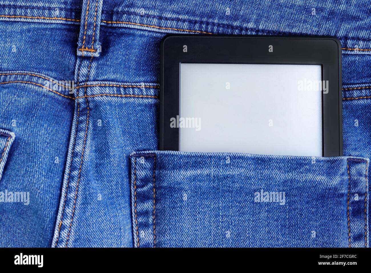 Ein modernes schwarzes elektronisches Buch mit einem leeren leeren Bildschirm in der Gesäßtasche einer leuchtend blauen Jeans. Mockup-Tablett Stockfoto