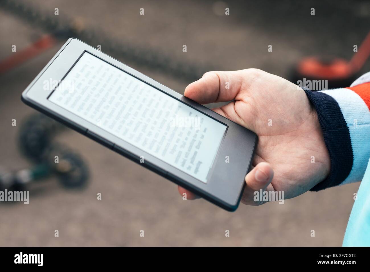 Männliche Hand mit modernem grauen elektronischen Buch. Bücher überall mit einem Taschenleser oder Tablet lesen. Selektiver Fokus. Nahaufnahme. Unscharfer Hintergrund Stockfoto