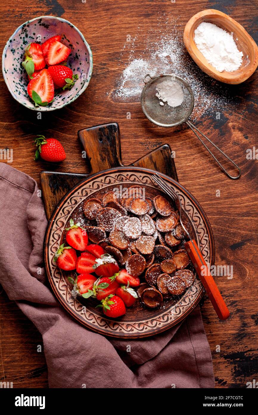 Mini-Schokolade Pfannkuchen Müsli mit Erdbeeren zum Frühstück auf alten Holztisch. Trendiges Frühstück mit winzigen Pfannkuchen. Draufsicht Stockfoto