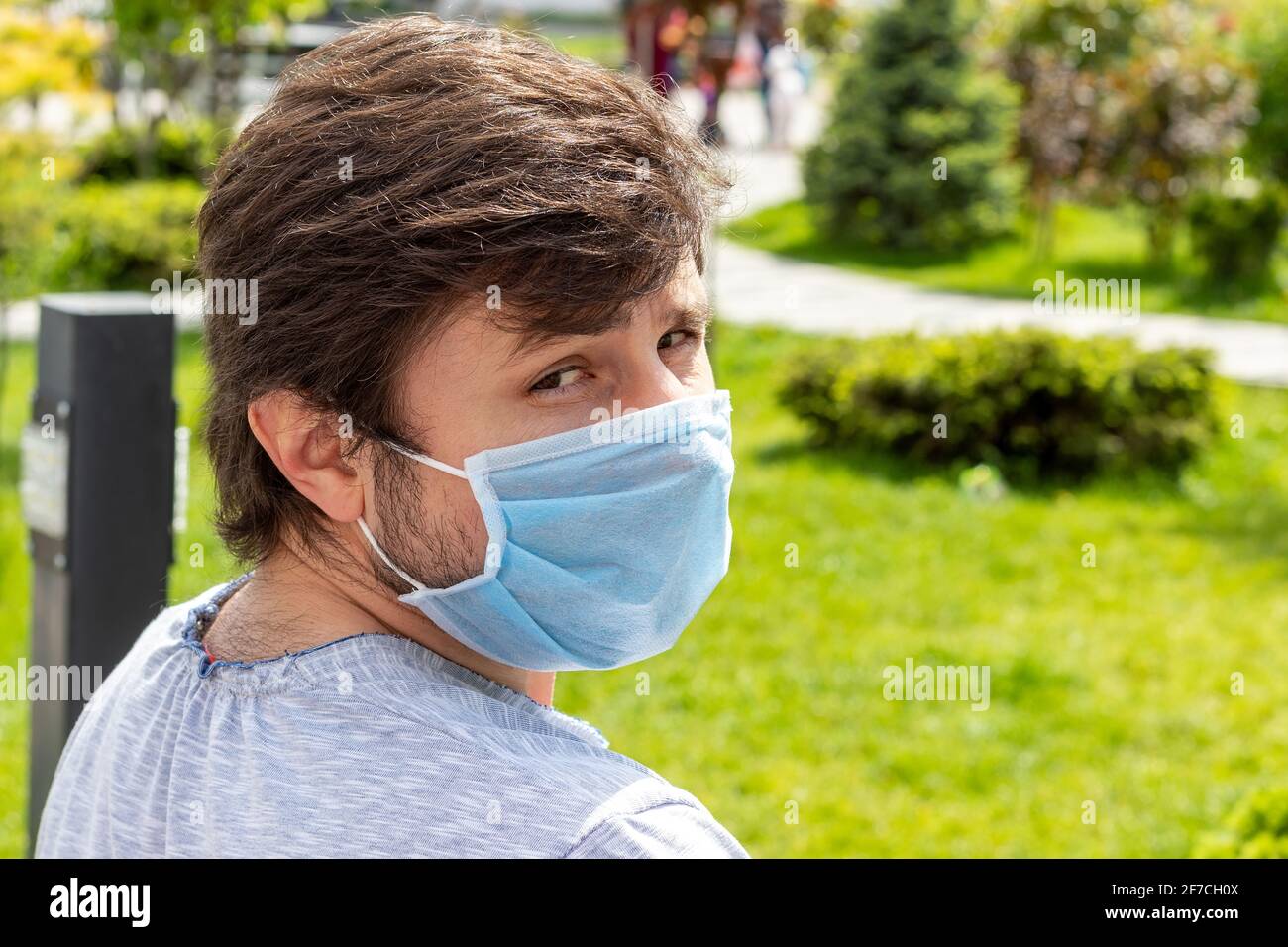 Porträt eines bärtigen Mannes in einer schützenden blauen medizinischen Maske vor einem verschwommenen Hintergrund im Freien. Männlich in einem Atemschutzgerät zum Schutz vor Infektionen mit Stockfoto