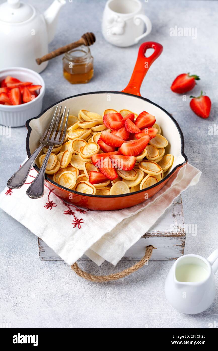 Mini weiße Pfannkuchen Müsli mit Erdbeeren in Bratpfanne zum Frühstück auf grauem Hintergrund. Trendiges Frühstück mit winzigen Pfannkuchen. Draufsicht Stockfoto
