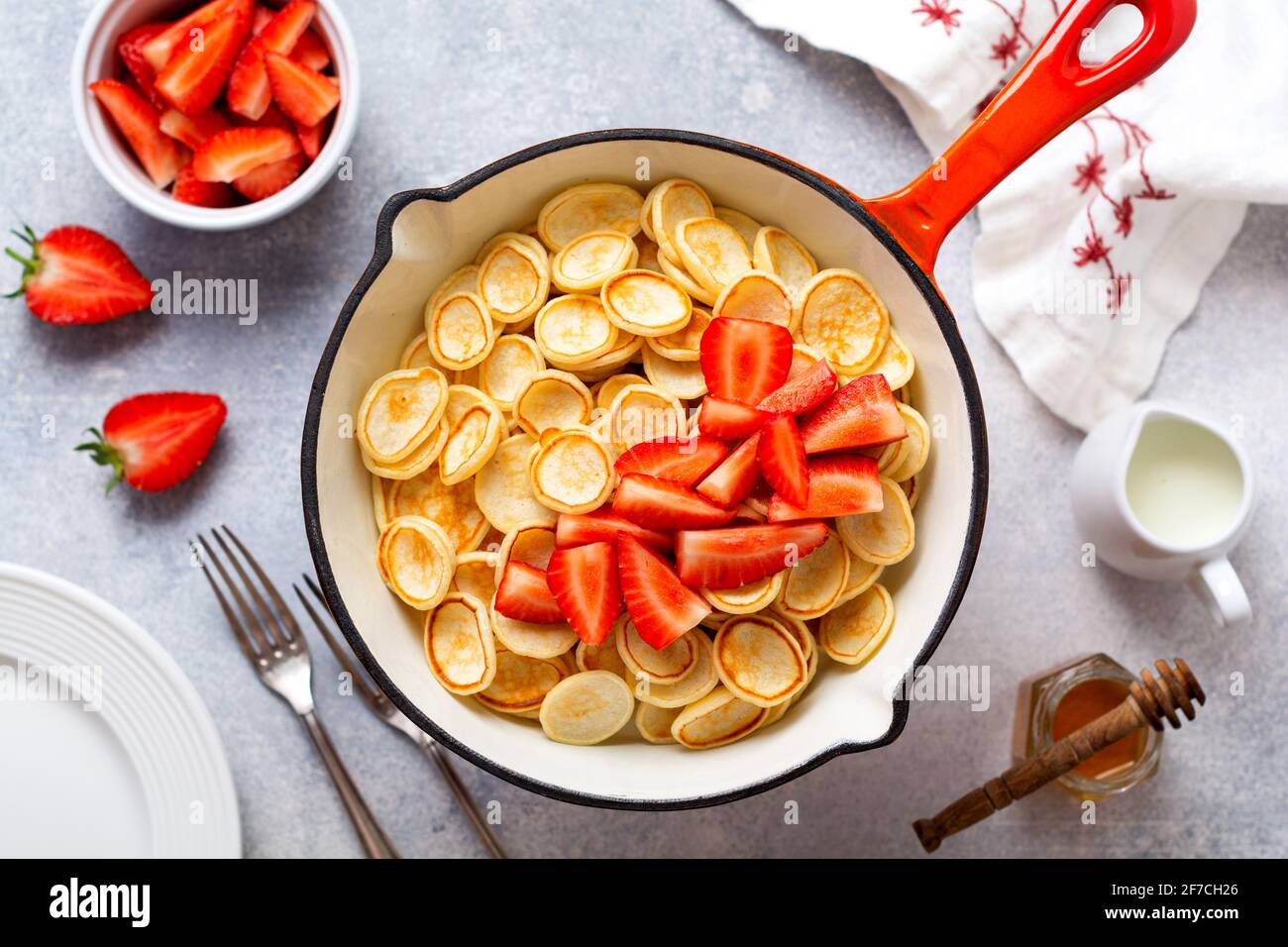 Mini weiße Pfannkuchen Müsli mit Erdbeeren in Bratpfanne zum Frühstück auf grauem Hintergrund. Trendiges Frühstück mit winzigen Pfannkuchen. Draufsicht Stockfoto