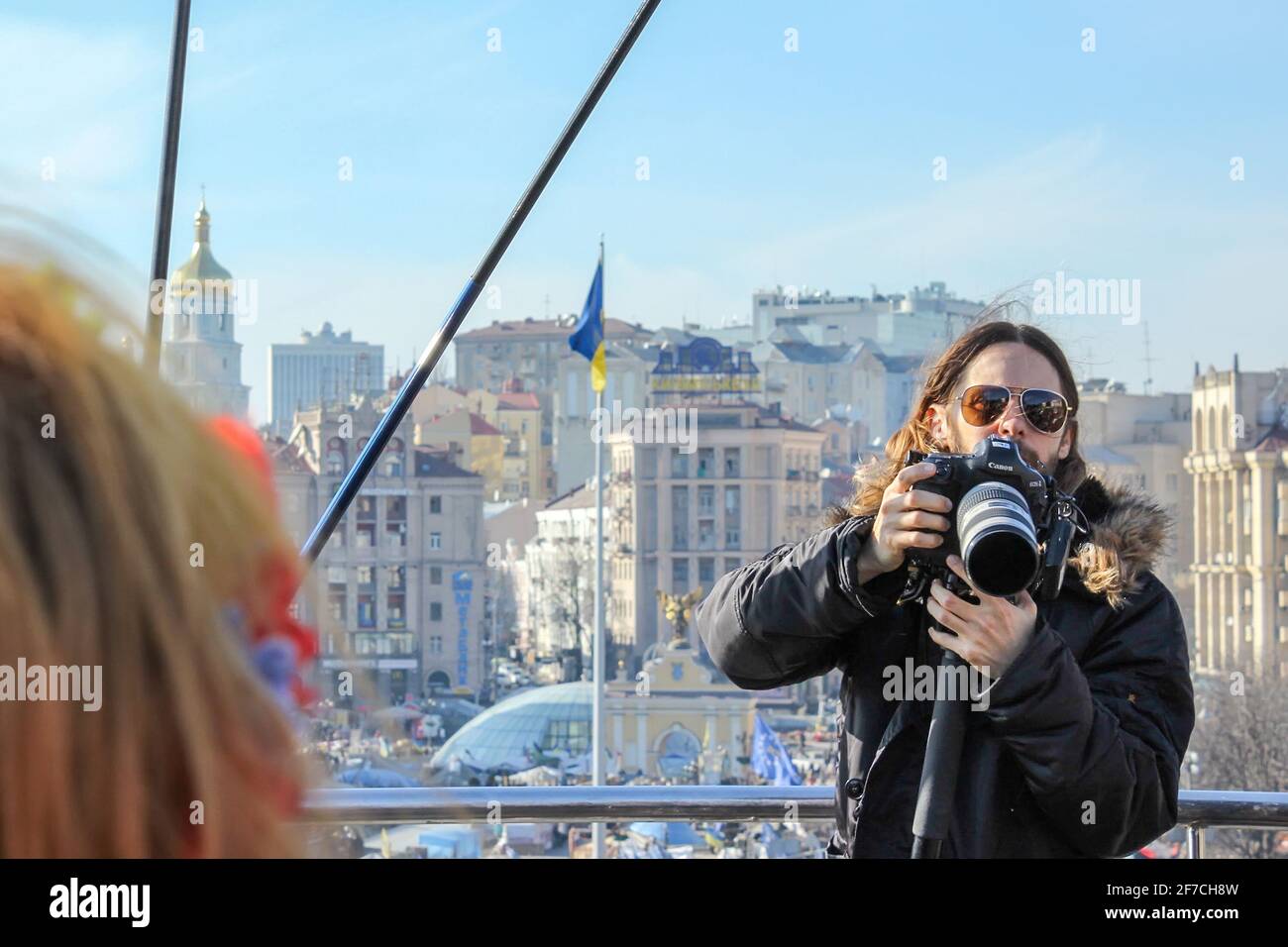 KIEW, UKRAINE - 13. MÄRZ 2014: Jared Leto mit einer Kamera, hinter seinem Rücken ist ein ausgebranntes Gebäude und eine Zeltstadt auf dem Maidan Nezalezhnosti zu sehen Stockfoto