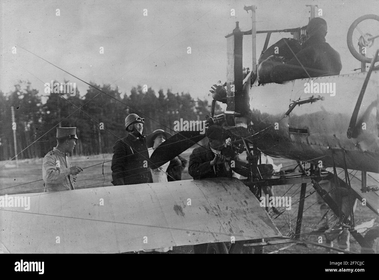 B 1 Bréguet C.U 1, 1915 Nahaufnahme des Flugzeugs B 1 Bréguet C.U 1 von hinten gesehen. Vor dem Flugzeug steht Henrik Hamilton im Airline-Helm und neben ihm seine Frau Ellen Hamilton. Ein Mechaniker arbeitet mit dem Flugzeug. Ein Mann sitzt auf dem Fahrersitz des Flugzeugs. Menschensammlung rund um das Flugzeug. Stockfoto