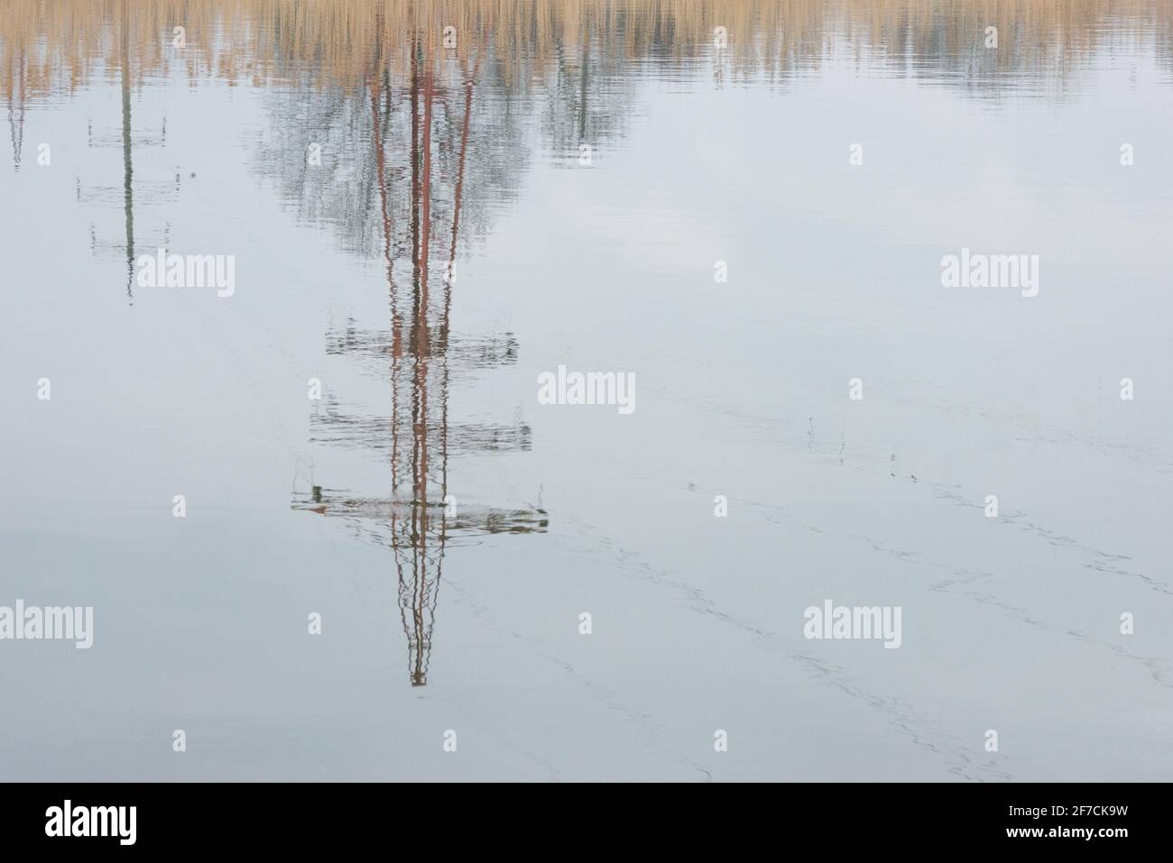 Reflexion eines Hochspannungsturms im Wasser dagegen Der Hintergrund des Schilfspannungsturms auf einem Hintergrund von Der Winterhimmel Stockfoto