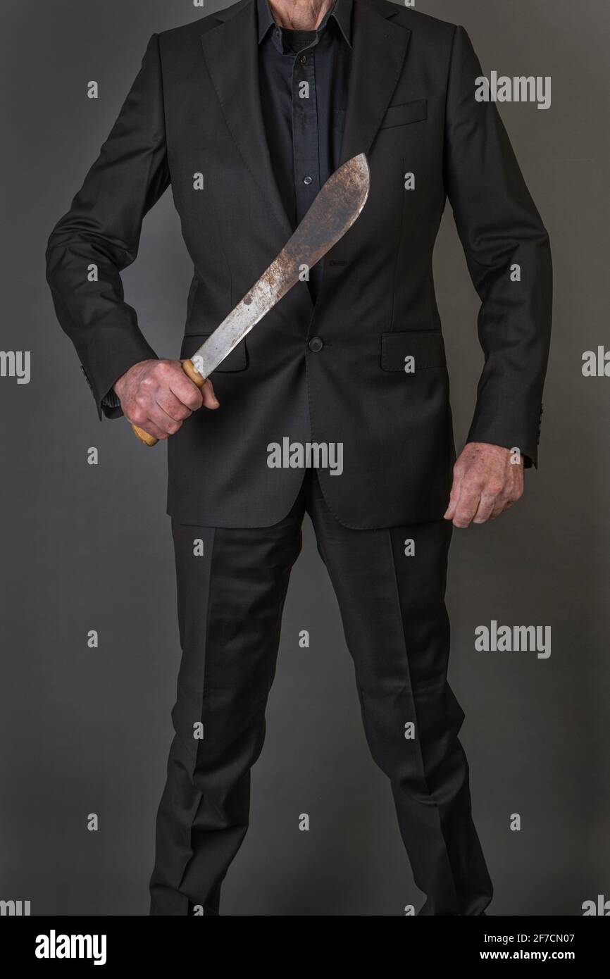 Ein Mann in einem schwarzen Anzug, der eine Machete in sich hält Eine bedrohliche Art und Weise Stockfoto
