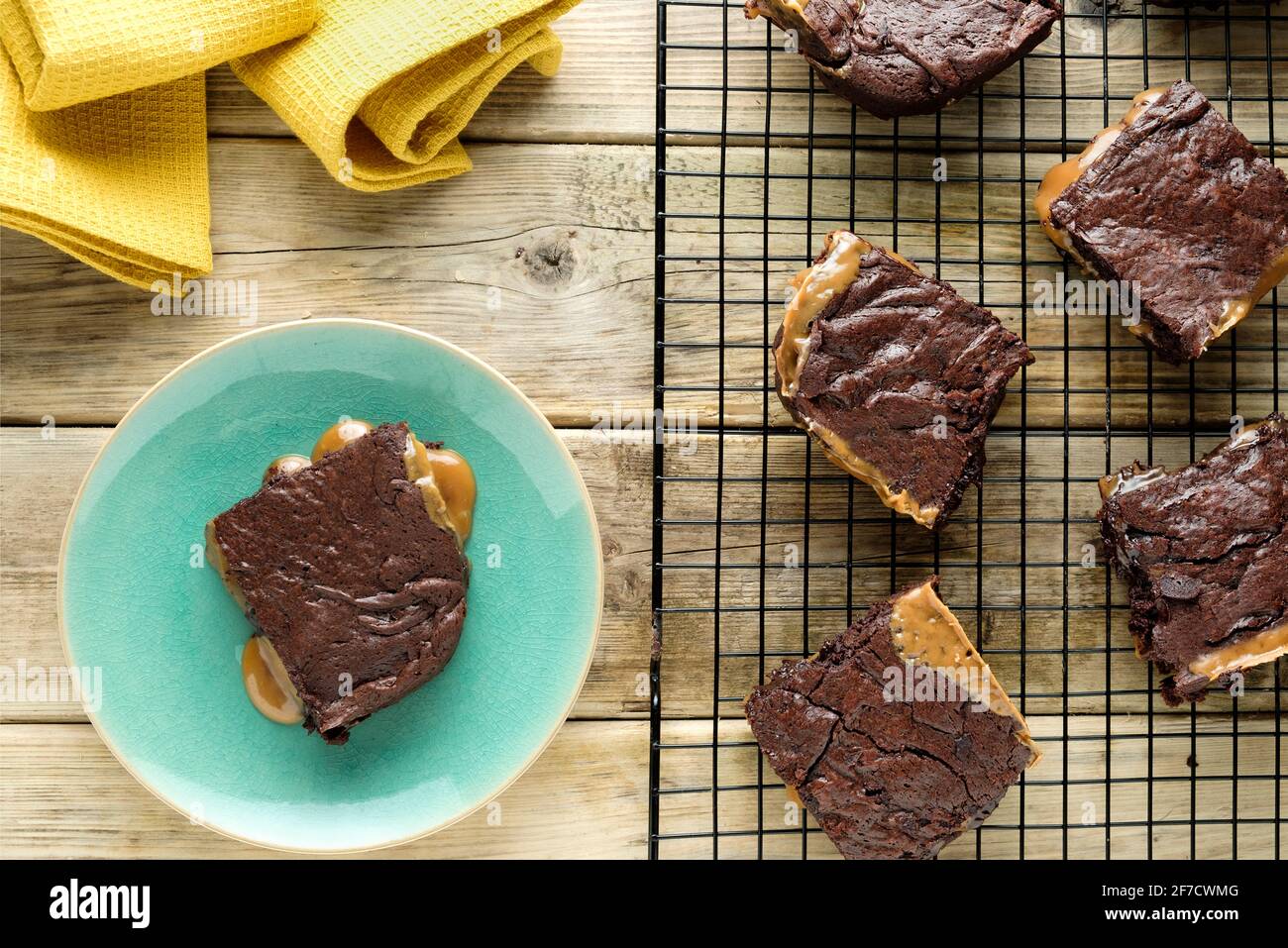 Eine frisch gekochte Charge gesalzener Karamell-Brownies, die auf einem Drahtgestell abkühlen. Ein Brownie ist überzogen und sickelt geschmolzenes Karamell auf den Teller Stockfoto