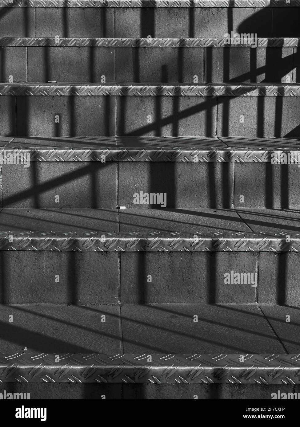 Eine banale, aus Keramik geflieste Treppe in Nahaufnahme, abstrakt durch die scharfen Schattenbalken, die vom starken Frühlingssonne gegossen werden. Stockfoto