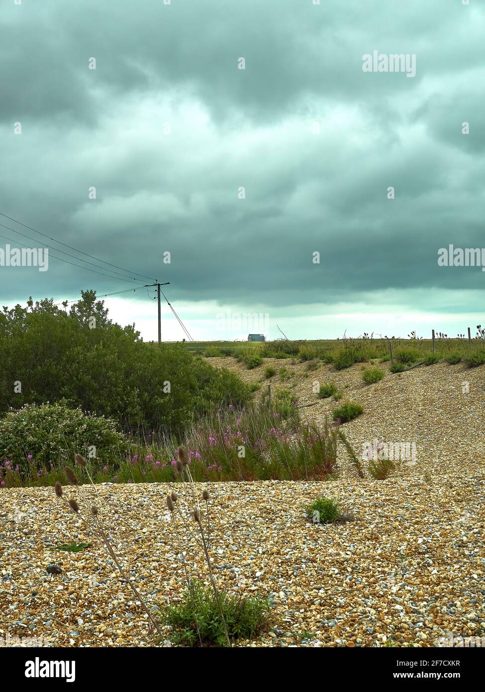 Verlassene Landschaft mit einem geschwungenen Kiesufer, das mit einem silhouettierten Telegrafenmast und einer verlassenen Rettungsbootstation zum Horizont zurückkehrt. Stockfoto