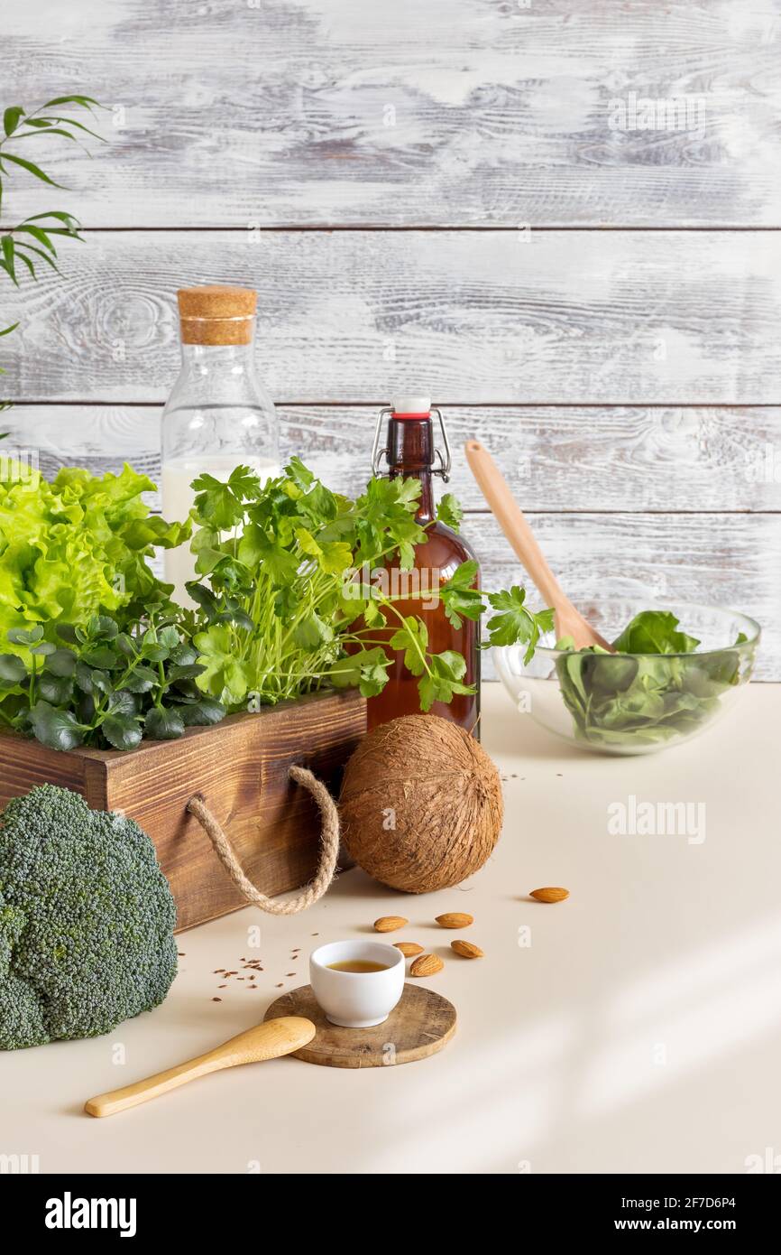 Zusammensetzung von gesunden veganen Lebensmitteln in einer umweltfreundlichen Küche. Natürliches, biologisches, grünes Gemüse, frische Kräuter, Nussmilch auf Holzgrund Stockfoto