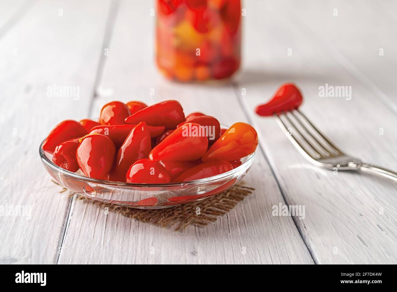 Eingelegte rote Paprika auf einer Glasuntertasse über einem weißen Holztisch. Marinierte Paprika-Schoten aus nächster Nähe. Fermentiertes Bio-Gemüse. Stockfoto