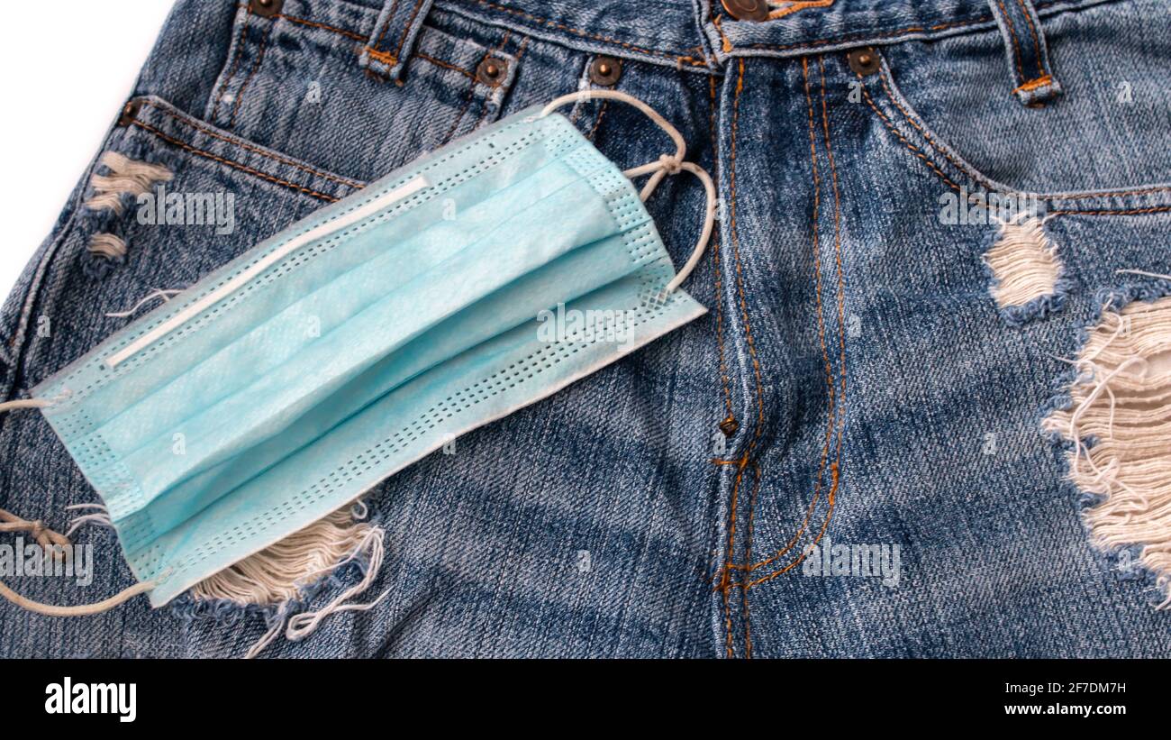 Eine OP-Maske, die im Februar 2021, einem Jahr nach der COVID-19-Pandemie, auf einem Paar beklemmter blauer jean-Shorts aufliegt. Stockfoto