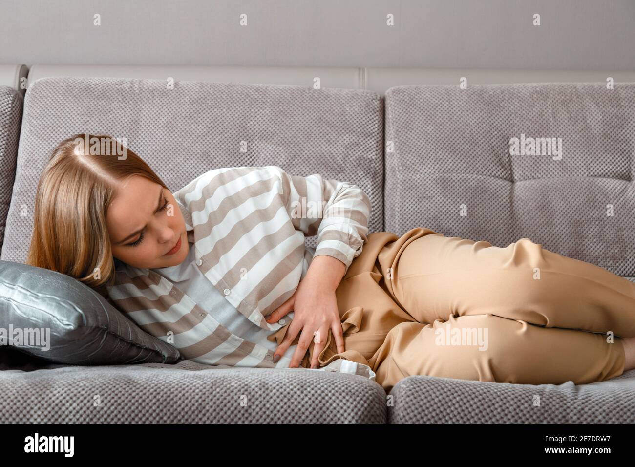 Die junge Frau hat Bauchschmerzen, die am Arbeitstag im Büro auf der Couch liegen. Akute Schmerzen bei aufblähender pms. Teenager-Mädchen mit Schmerzen Probleme Darmkrankheit. Stockfoto