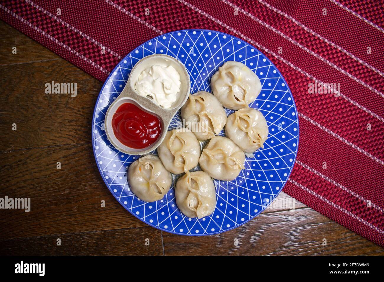 manti und Sauce auf einem blauen Teller auf einem Burgund Hintergrund Stockfoto