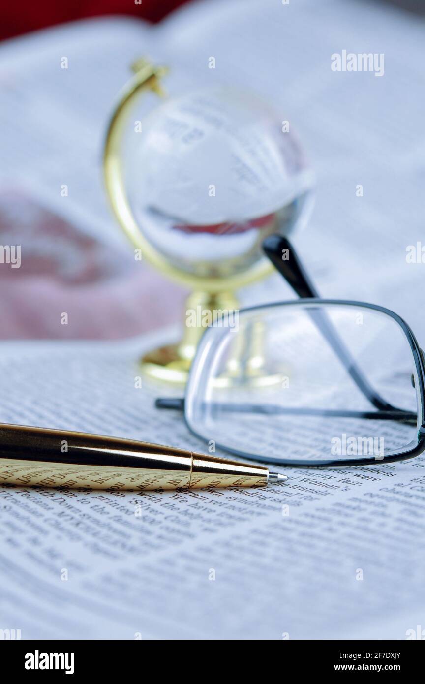Brille, Stift, Globus liegen auf einer Zeitung Stockfoto