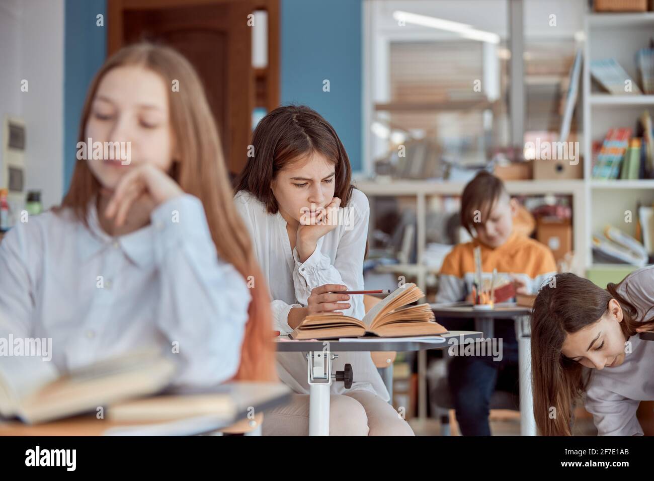 Junges Mädchen sieht abwesend im Lesen. Grundschüler sitzen auf Schreibtischen und lesen im Klassenzimmer Bücher Stockfoto