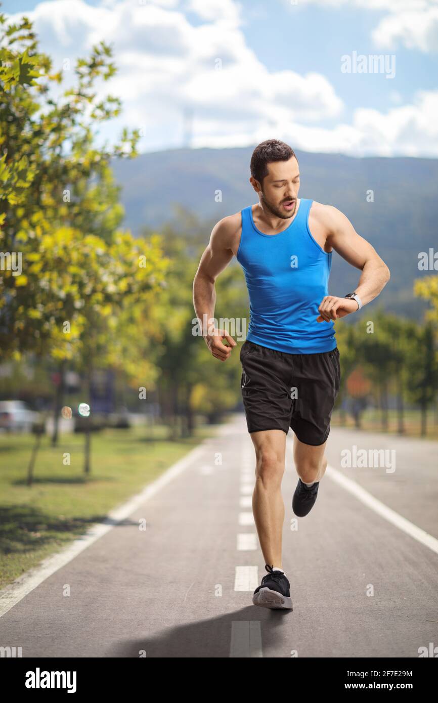 Porträt eines männlichen Läufers in voller Länge, der die Zeit überprüft Ein Laufpfad Stockfoto