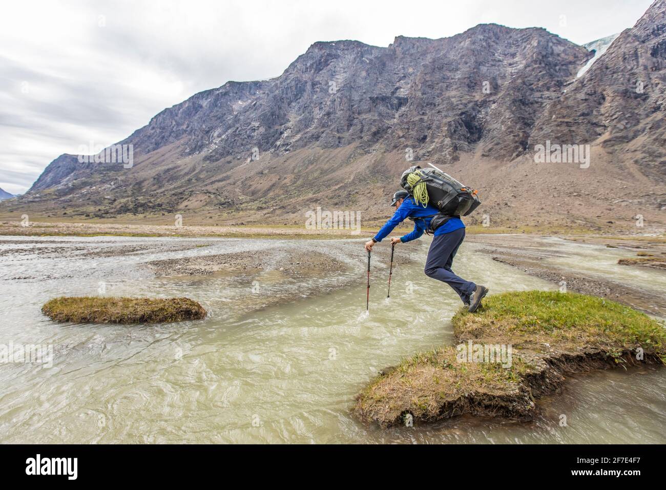 Backpacker nutzt Trekkingstöcke, um über einen tiefen Fluss zu springen Kanal Stockfoto
