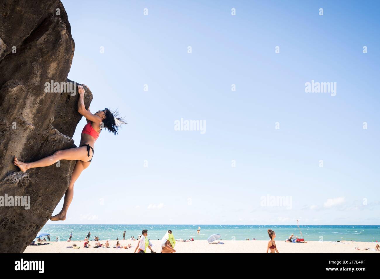 Wagemutige Dame, die einen Felsblock ohne Geschirr auf einem skaliert Sonniger Strand in Oahu Stockfoto