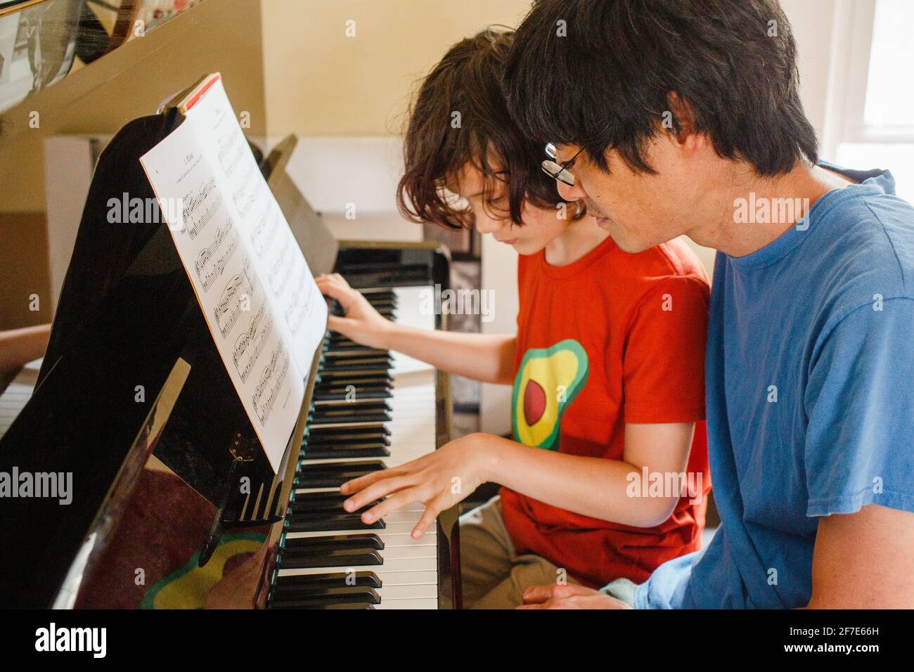 Ein Junge und ein Vater sitzen beim Klavierspielen eng beieinander Musik zu Hause Stockfoto