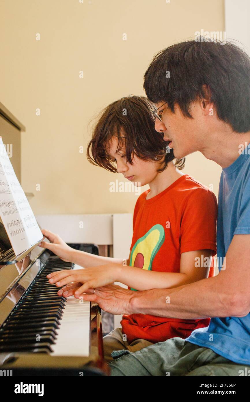 Ein Vater und ein Sohn sitzen beim Klavierbau eng beieinander Musik Stockfoto