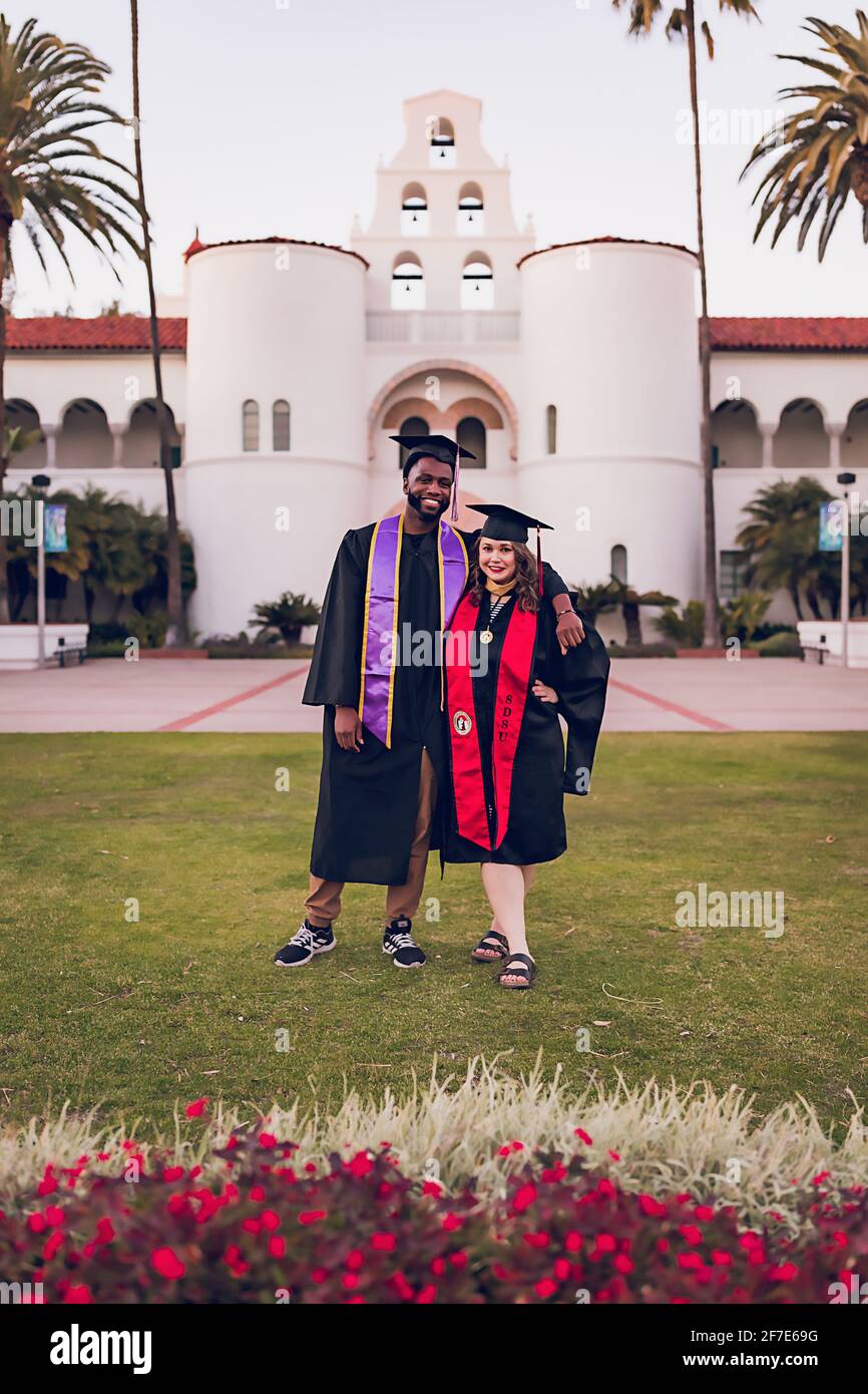 Mann und Frau tragen ein Abschlusskleid/-Mütze und umarmen sich. Stockfoto