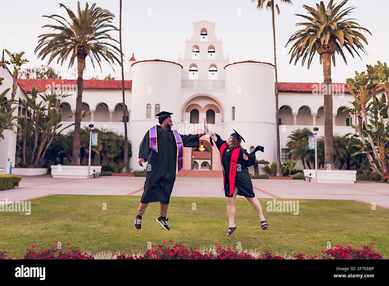 Mann und Frau springen, tragen ein Abschlusskleid/Mütze. Stockfoto