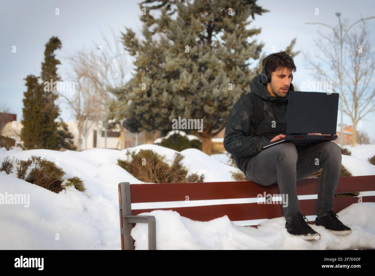 Dunkelhaariger, tausendjähriger College-Junge, der mit Kopfhörern auf einem Laptop studiert Stockfoto