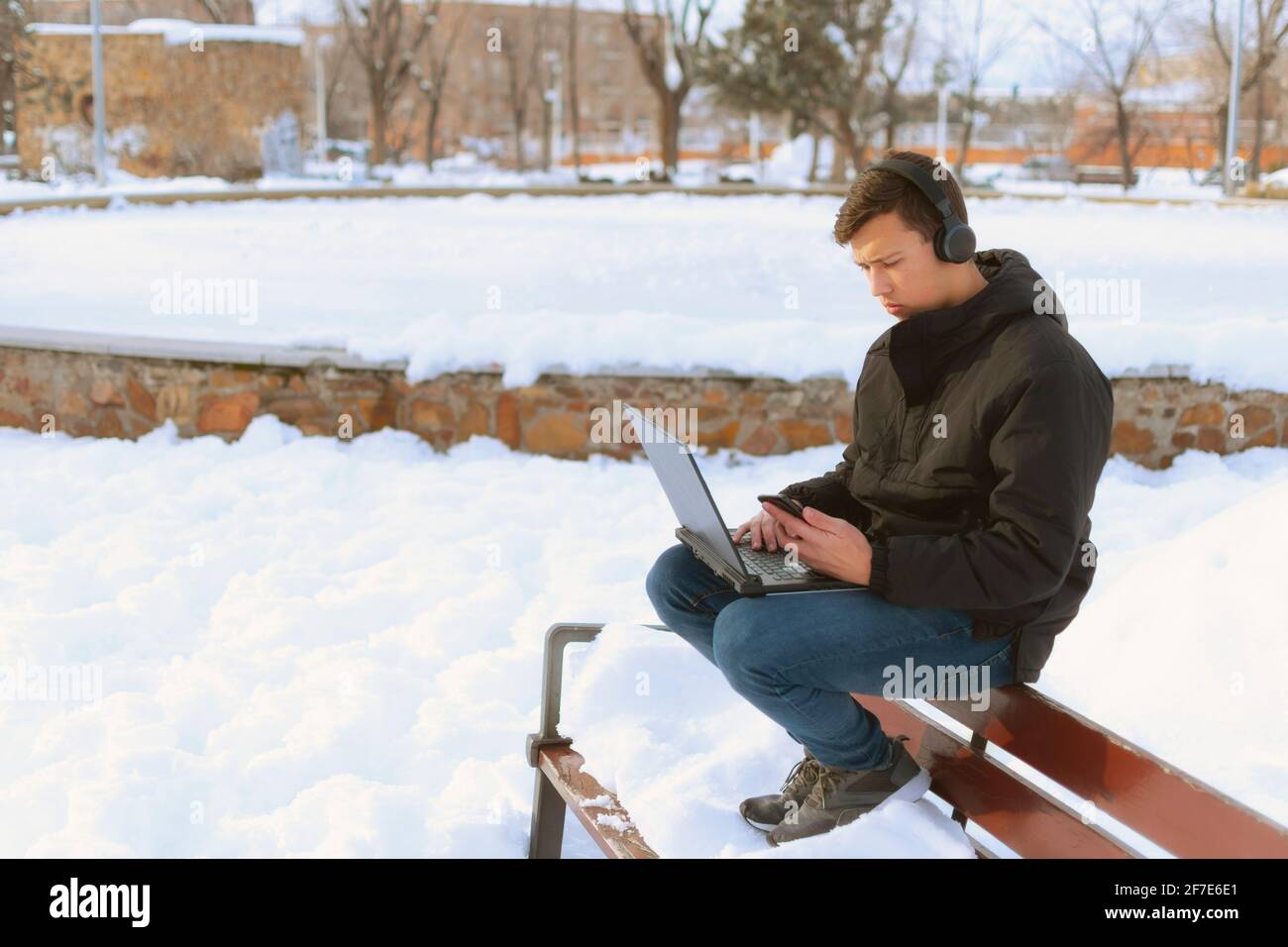 Millennial College Boy, der im Park auf einem Laptop mit Kopfhörern studiert Stockfoto