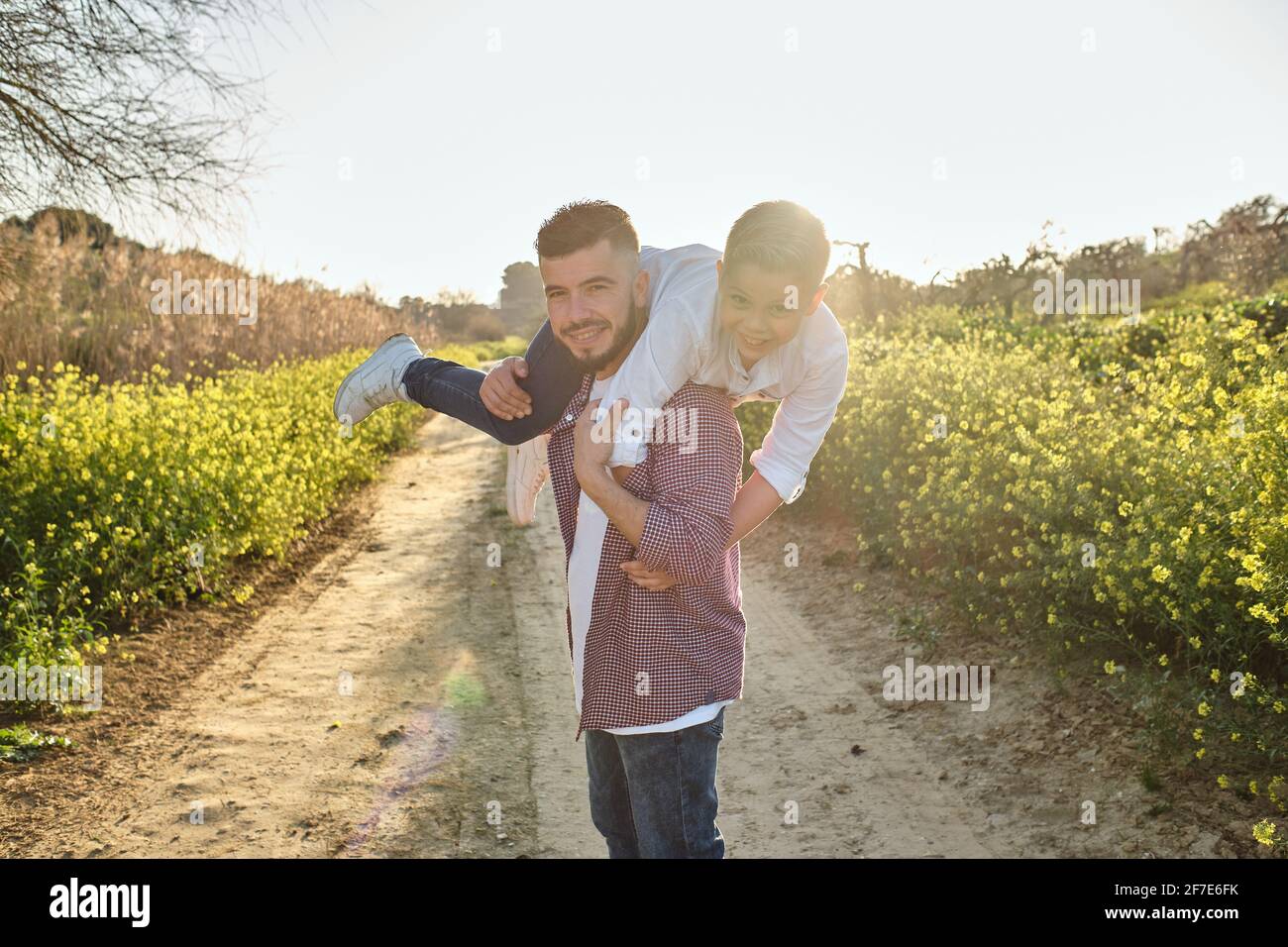 Glücklicher Vater schaut auf die Kamera, während er mit seinem Sohn spielt Auf dem Feld Stockfoto