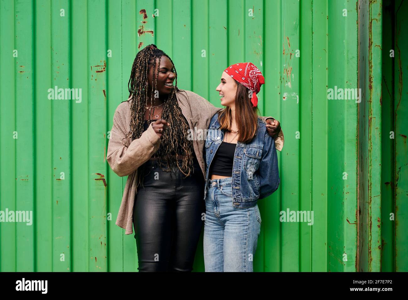 Zwei multiethnische Frauen in Stadtkleidung lächeln und umarmen jede Andere Stockfoto