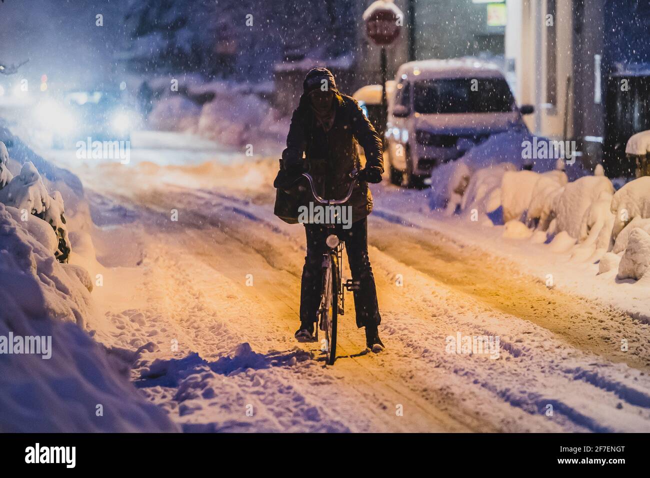 Eine Frau, die in den frühen Morgenstunden im Schnee auf der Straße der Stadt mit dem Fahrrad unterwegs ist. Pendeln mit dem Fahrrad bei kaltem und verschneiten Wetter. Stockfoto
