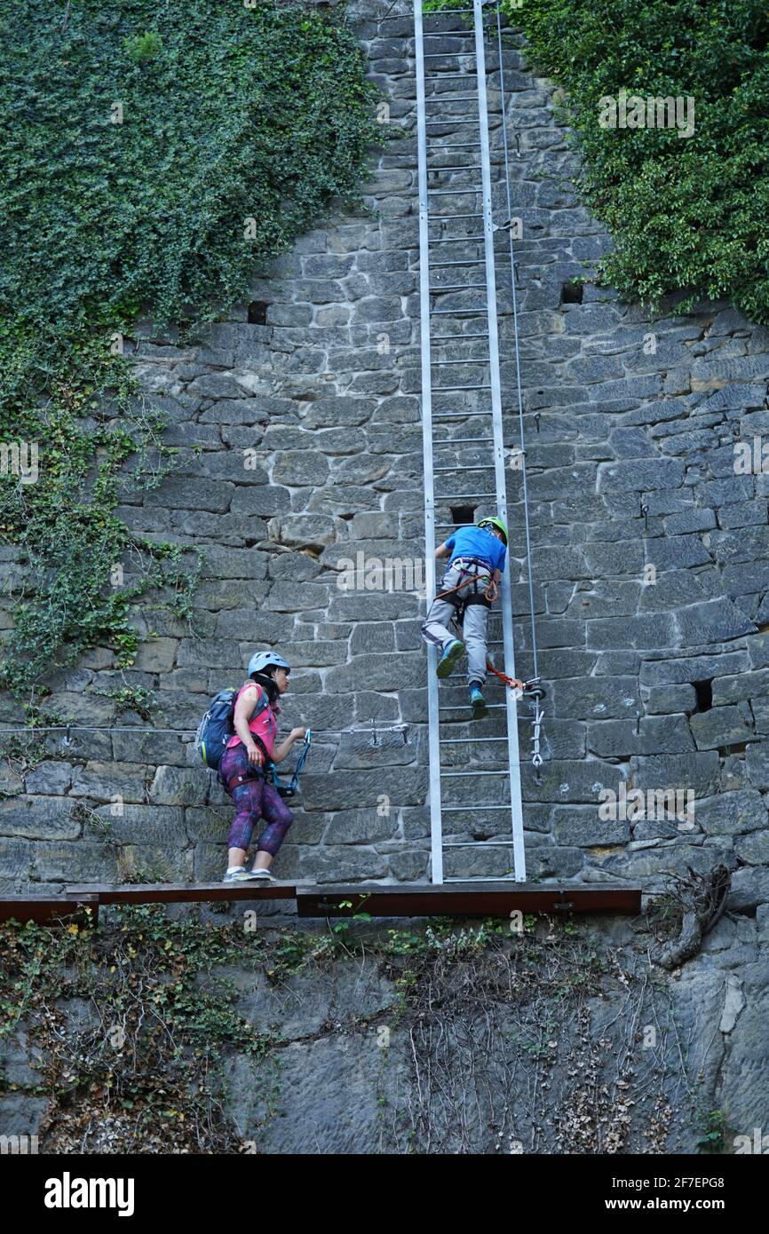 Decin, Tschechische Republik - Mai 7 2020: Mutter beobachtet ihren jungen Sohn beim Klettern einer steilen Leiter auf Klettersteig, Familienaktivitäten im Freien Stockfoto