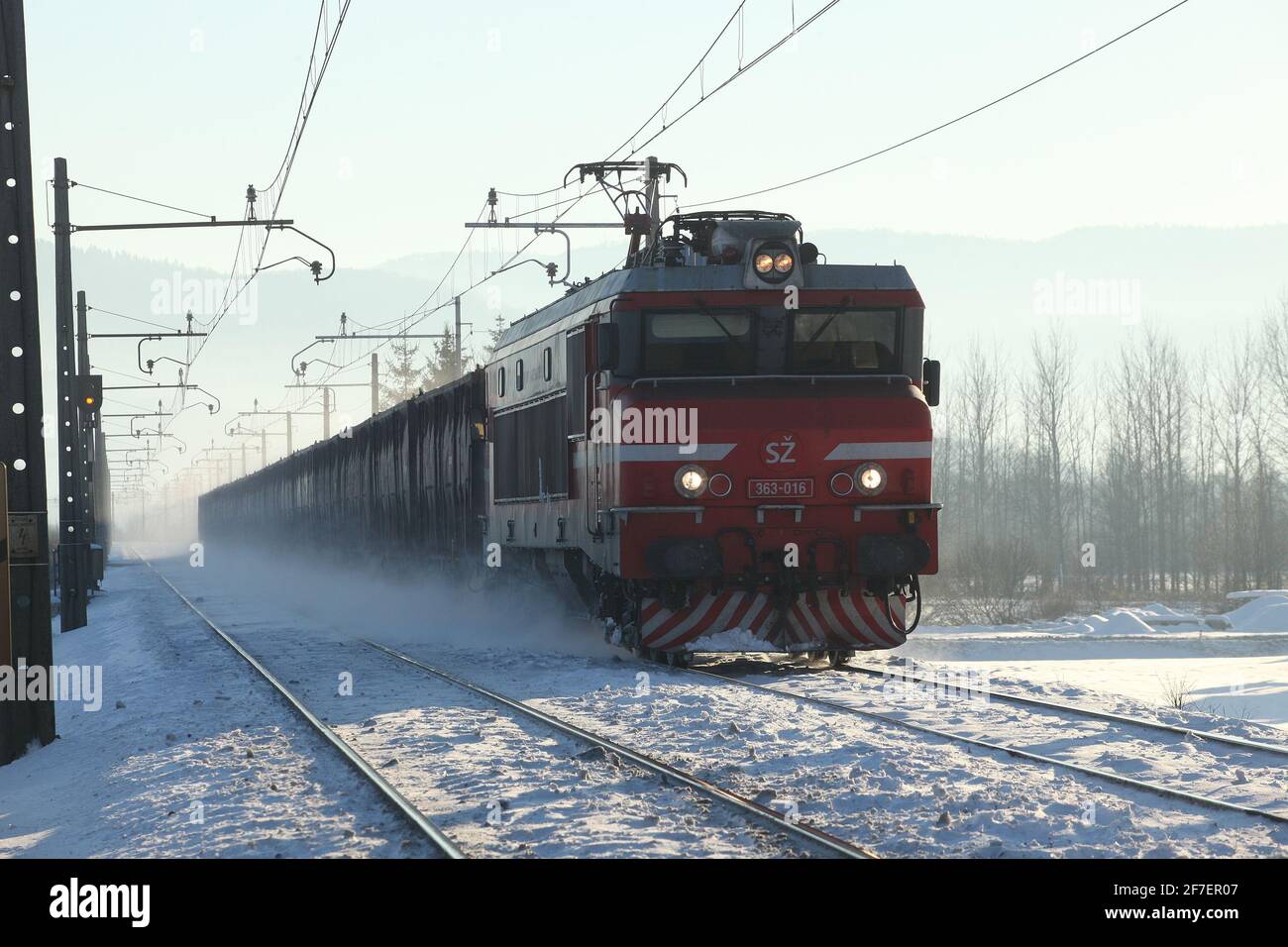 Ein Zug, der auf einer verschneiten Strecke auf die Kamera zufährt und Schnee vom Boden aufsteigt. Stockfoto