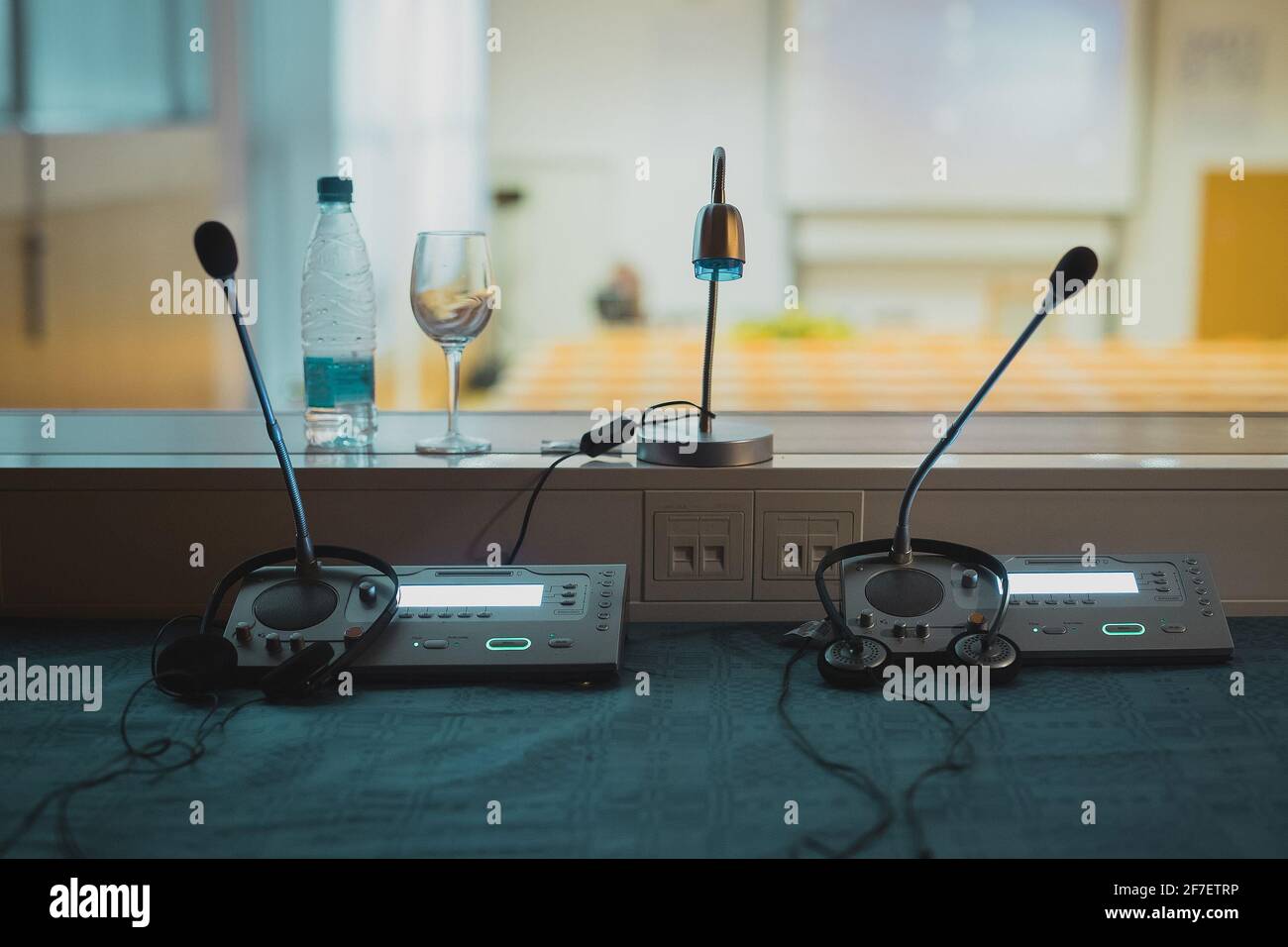Innerhalb der Übersetzungs- oder Dolmetschkabine. Schreibtisch mit Mikrofonen und Audioplatine, mit sichtbarem Konferenzsaal im Hintergrund. Stockfoto
