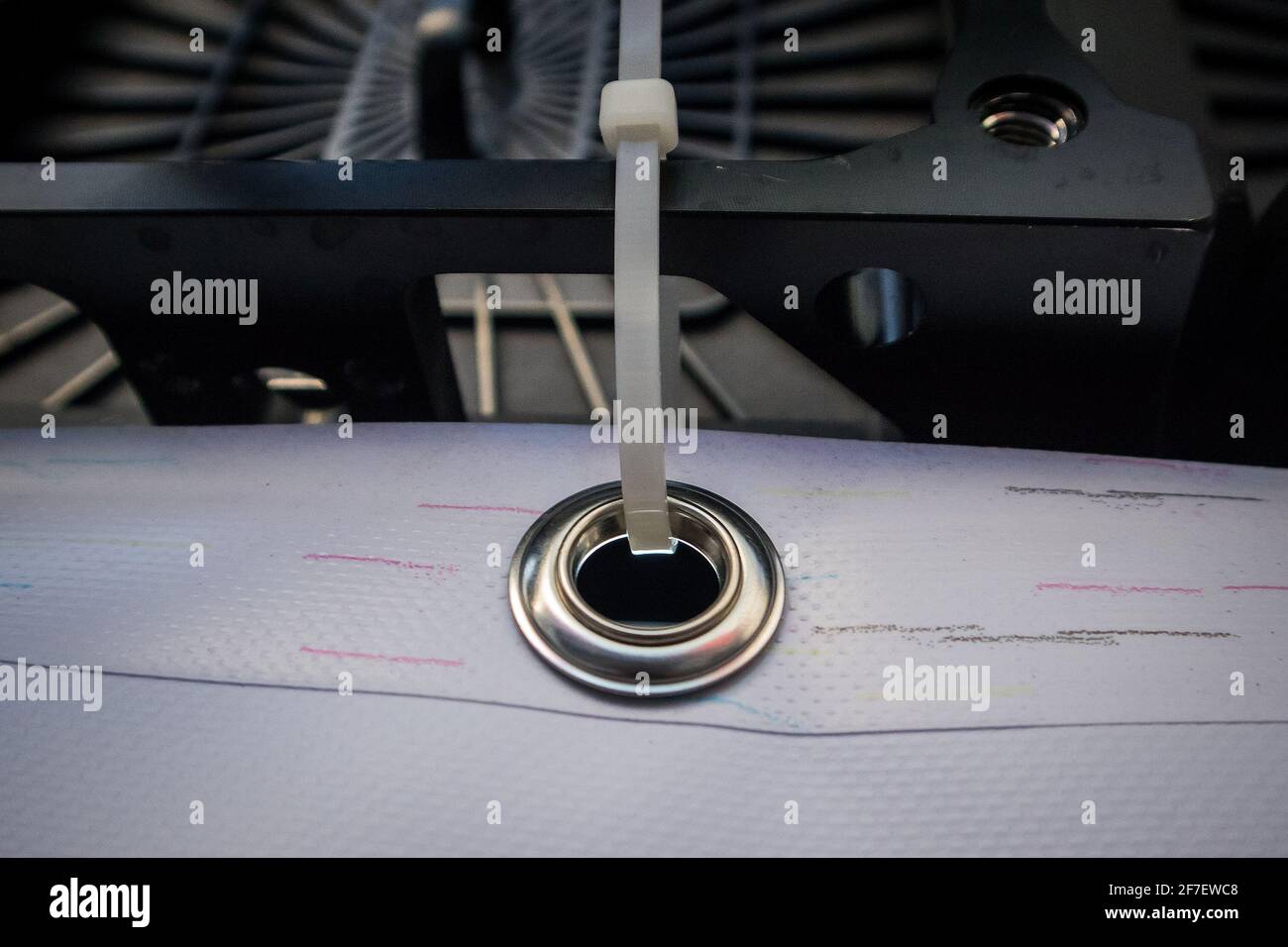 Metallring oder Tülle auf einem Vinyl-Banner, mit einem Reißverschlussband gesichert. Genietete Stahlöse zum Aufhängen von Bannern, Detail mit Reißverschluss. Stockfoto