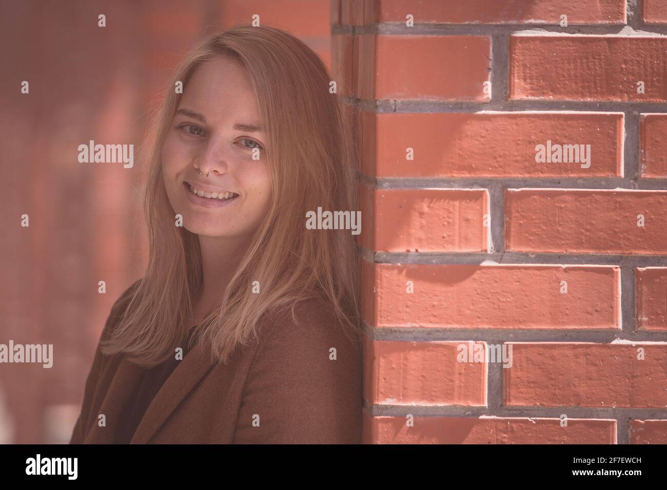 Nette, modische junge Frau in einem roten Backsteinflur, die auf die Kamera blickt. Kaukasisches Mädchen mit Septumpiercing in einem Let's go-Modus, das tras will Stockfoto