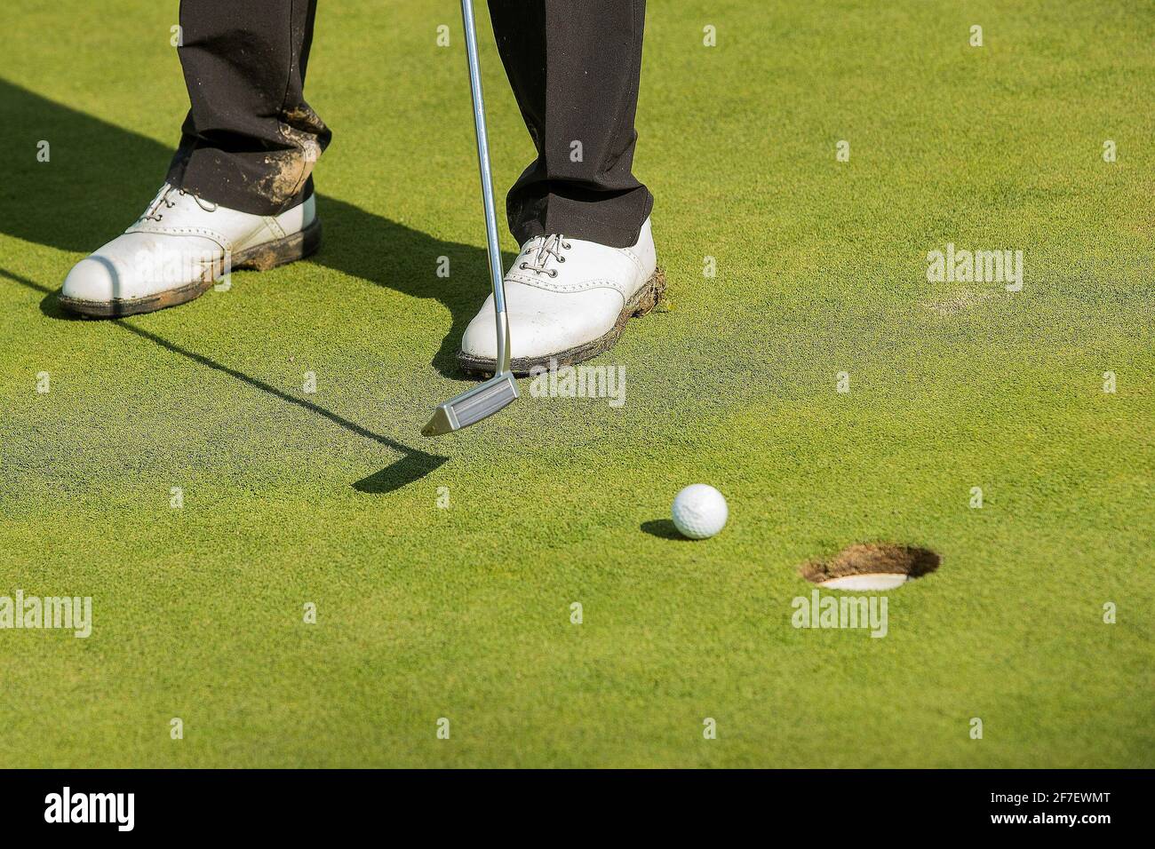 Schmutzige und schlammige Golfschuhe an einer Person, die einen Golfschläger hält. Stockfoto