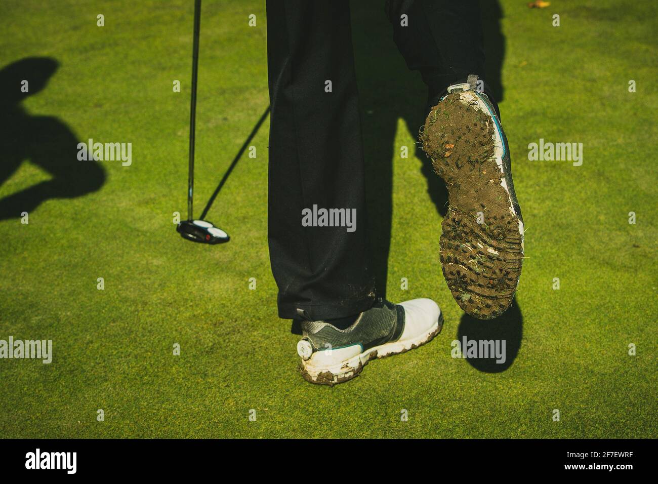 Schmutzige und schlammige Golfschuhe an einer Person, die einen Golfschläger hält. Stockfoto